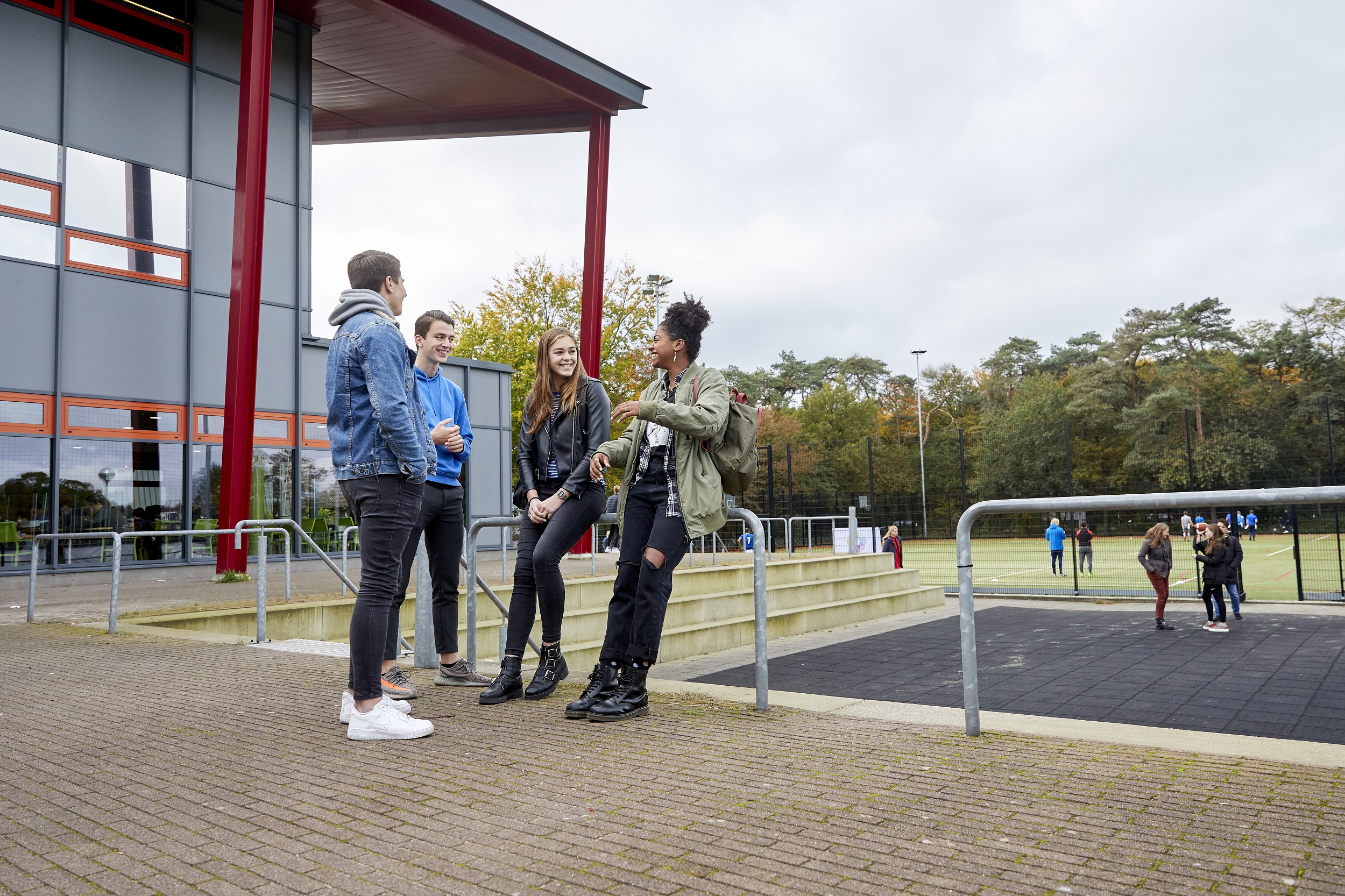 Twee jongens en twee meisjes staan op een schoolplein met elkaar te praten