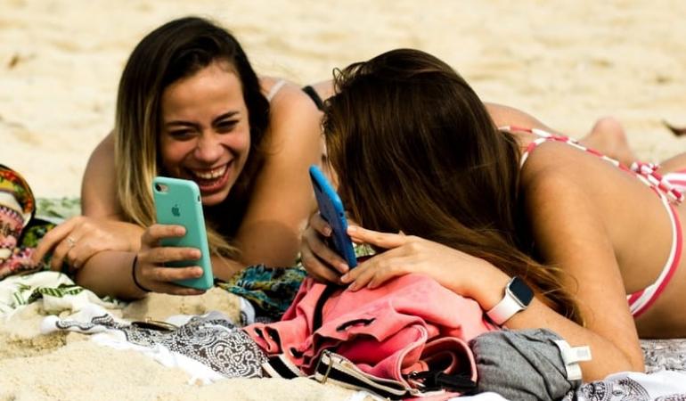 Decoratieve foto van twee vriendinnen die op het strand liggen en met elkaar lachen